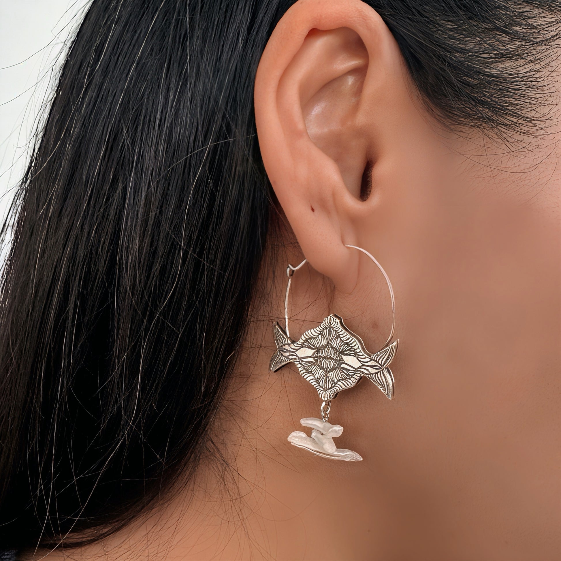 Silver hoop earring with intricate design  and freshwater pearls worn by a person