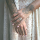 Close-up of hands with tattoos  and a silver decorative ring against a lace curtain background