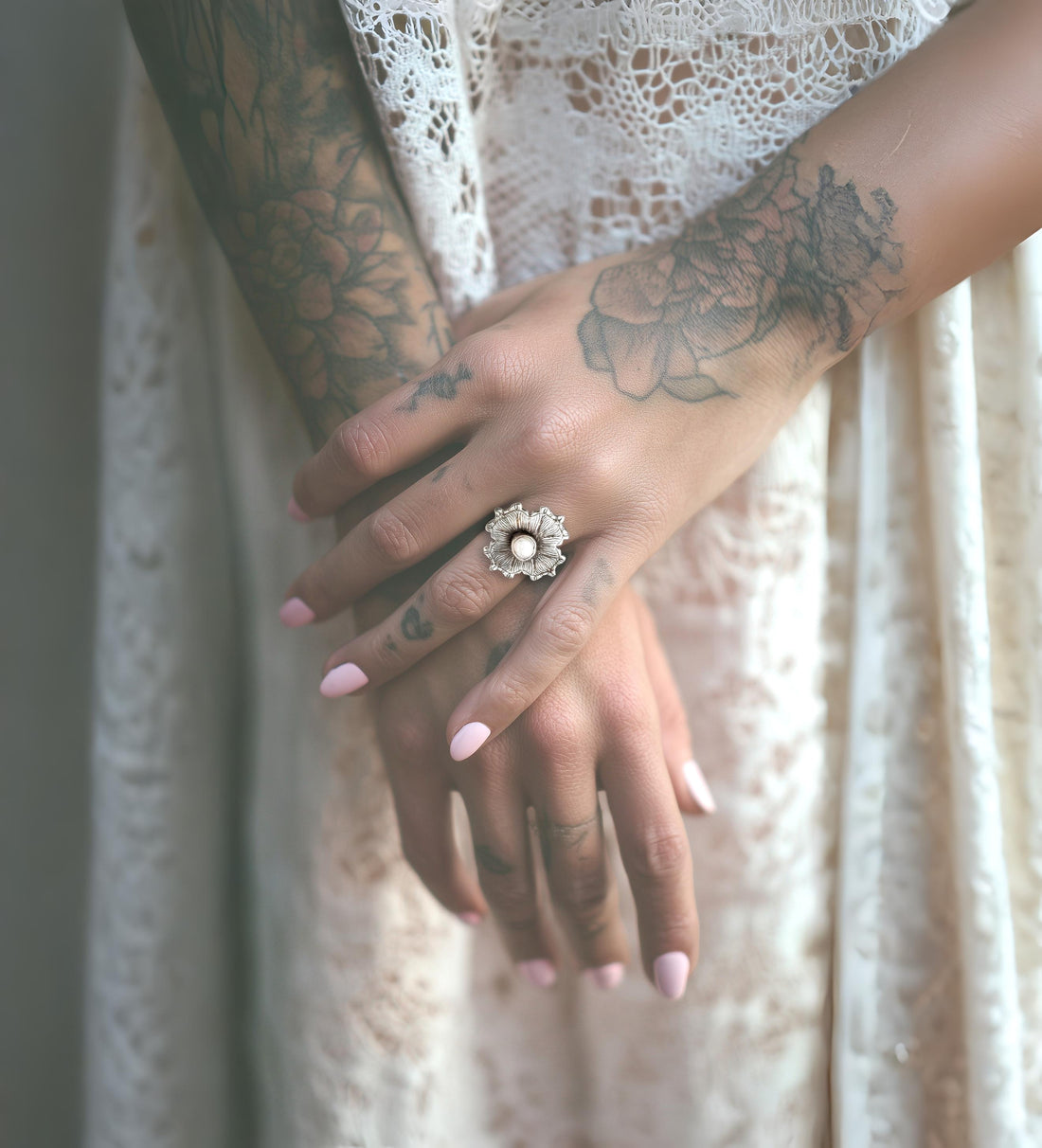 Close-up of hands with tattoos  and a silver decorative ring against a lace curtain background