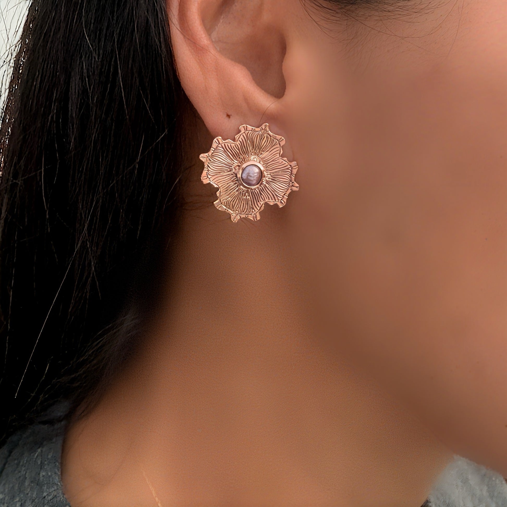 Close-up of a person wearing a rose gold floral earring.