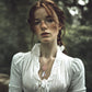 Woman with red hair and freckles wearing a white blouse and a rose gold pendant in a forest setting