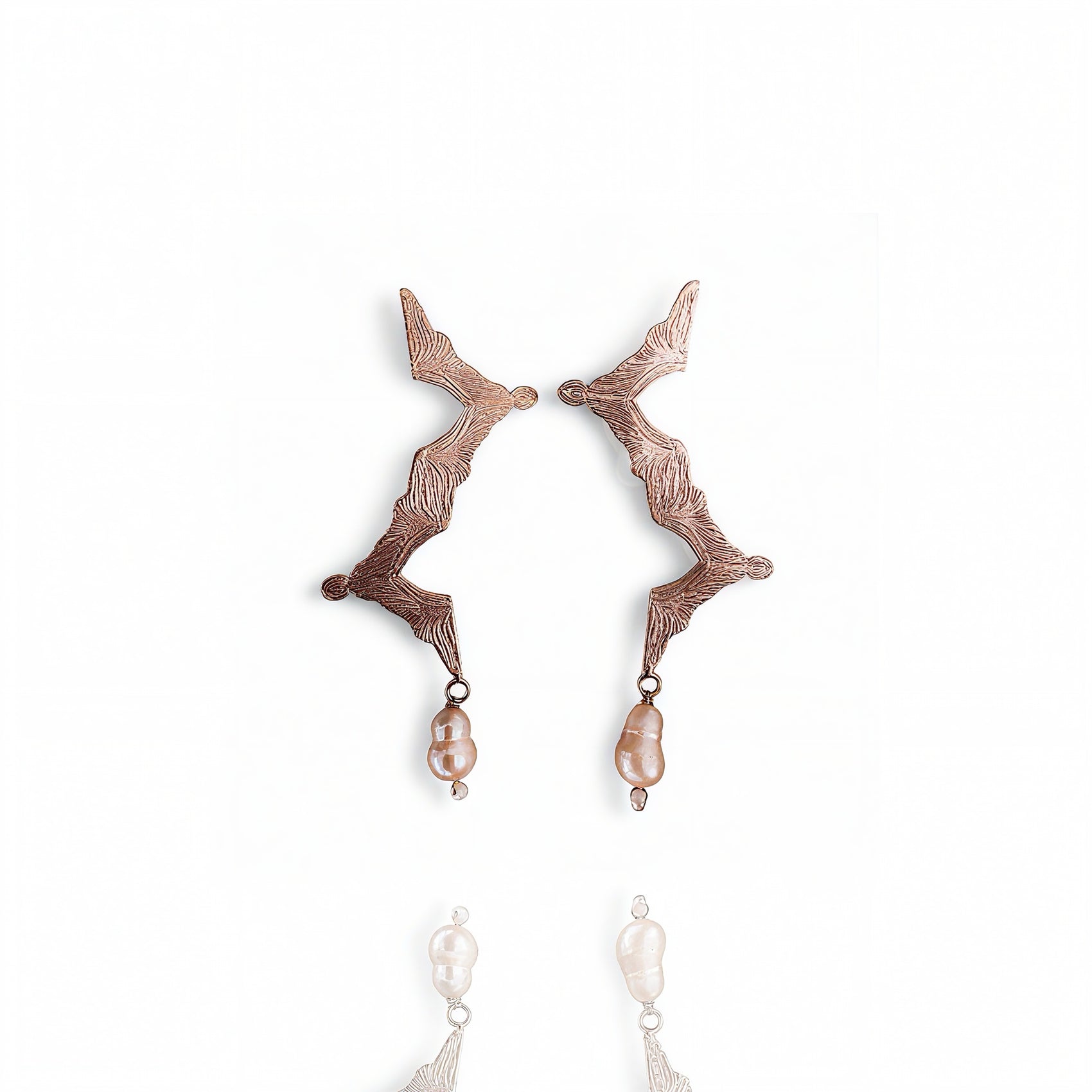 Pair of rose gold earrings with pearl drops on a white background