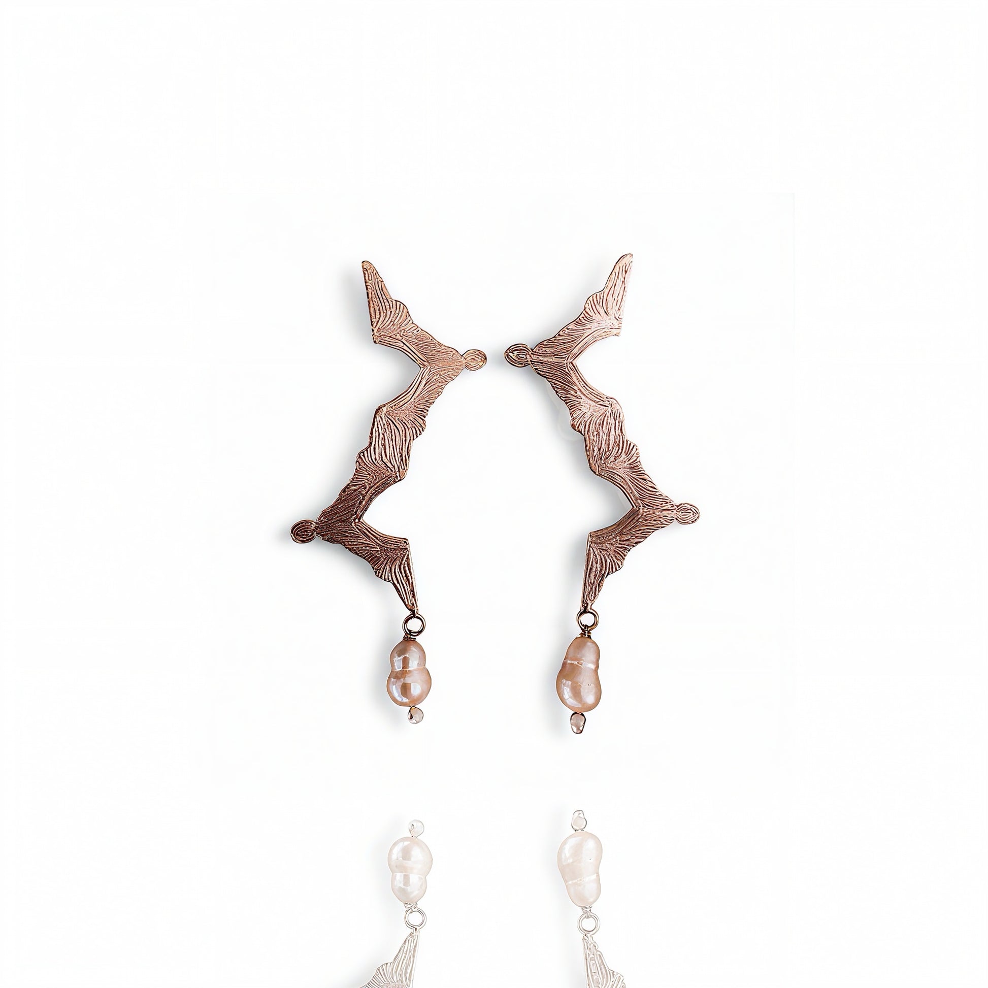 Pair of rose gold earrings with pearl drops on a white background