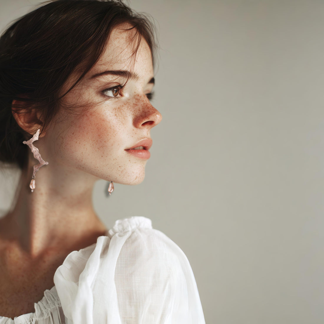 Woman wearing a white blouse with floral earrings against a neutral background
