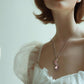 Woman wearing a delicate necklace with a pink pendant against a soft background