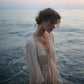 Woman in a flowing dress and rose gold necklace standing in water with a blurred background